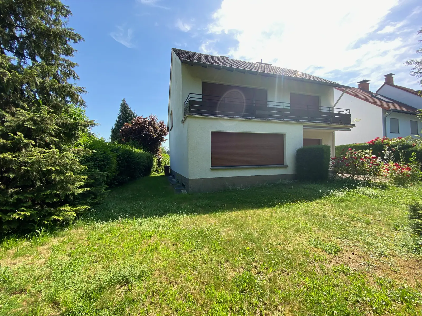 Garten mit Rasenfläche, Nadelbäumen und Blick auf die Westseite des Hauses mit Balkon